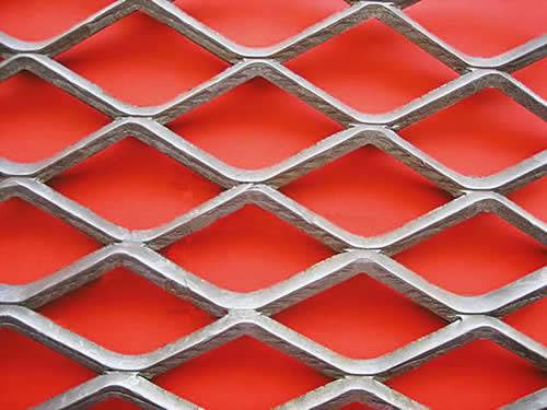 Fattened carbon steel expanded metal with diamond holes on red background.