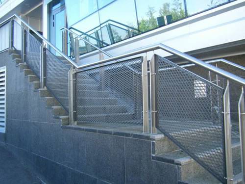 Expanded metal infill panels with diamond holes are installed on one side of broken-line stair railings outdoors.